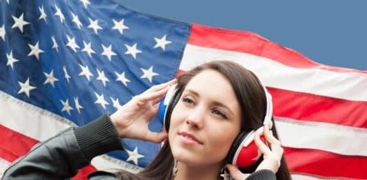 Menina com o seu fone de ouvido e a bandeira dos EUA de fundo representando a Sua meta é aprender inglês em 2025. Veja 13 dicas para tornar isso realidade!