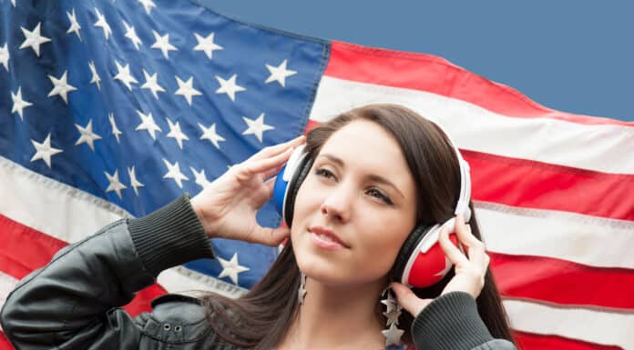 Menina com o seu fone de ouvido e a bandeira dos EUA de fundo representando a Sua meta é aprender inglês em 2025. Veja 13 dicas para tornar isso realidade!
