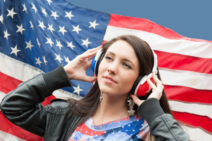 Menina com o seu fone de ouvido e a bandeira dos EUA de fundo representando a Sua meta é aprender inglês em 2025. Veja 13 dicas para tornar isso realidade!