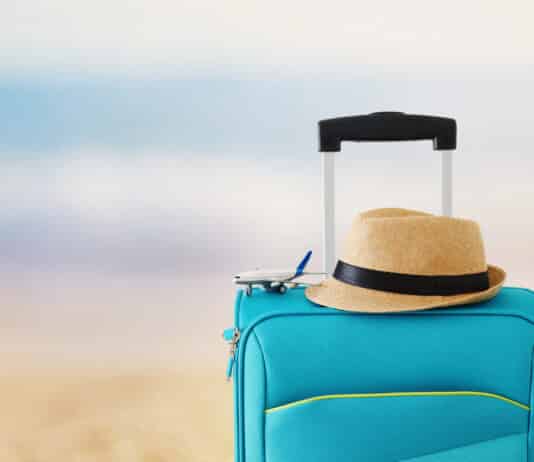 Férias e feriados em inglês: Como falar sobre datas festivas Imagem de uma mala em uma praia representando as férias e feriados em inglês