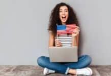 mulher sentada no chão com notebook no colo mostrando bandeira dos Estados Unidos