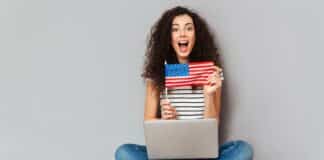 mulher sentada no chão com notebook no colo mostrando bandeira dos Estados Unidos
