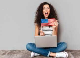 mulher sentada no chão com notebook no colo mostrando bandeira dos Estados Unidos