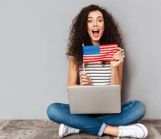 mulher sentada no chão com notebook no colo mostrando bandeira dos Estados Unidos