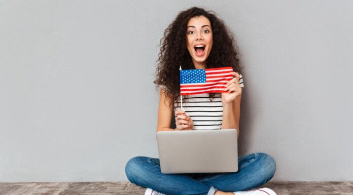 mulher sentada no chão com notebook no colo mostrando bandeira dos Estados Unidos