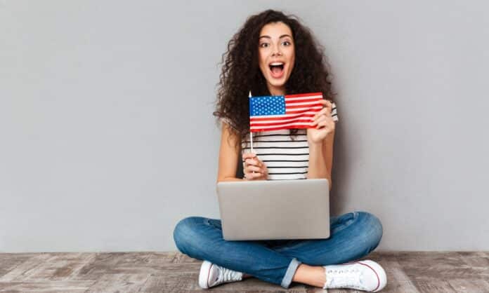 mulher sentada no chão com notebook no colo mostrando bandeira dos Estados Unidos