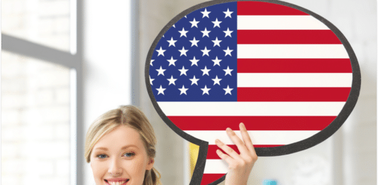 Has been, had been, have been: qual a diferença e como usar? Imagem de uma mulher segurando uma placa com a bandeira dos EUA representando os verbos: Has been, had been, have been